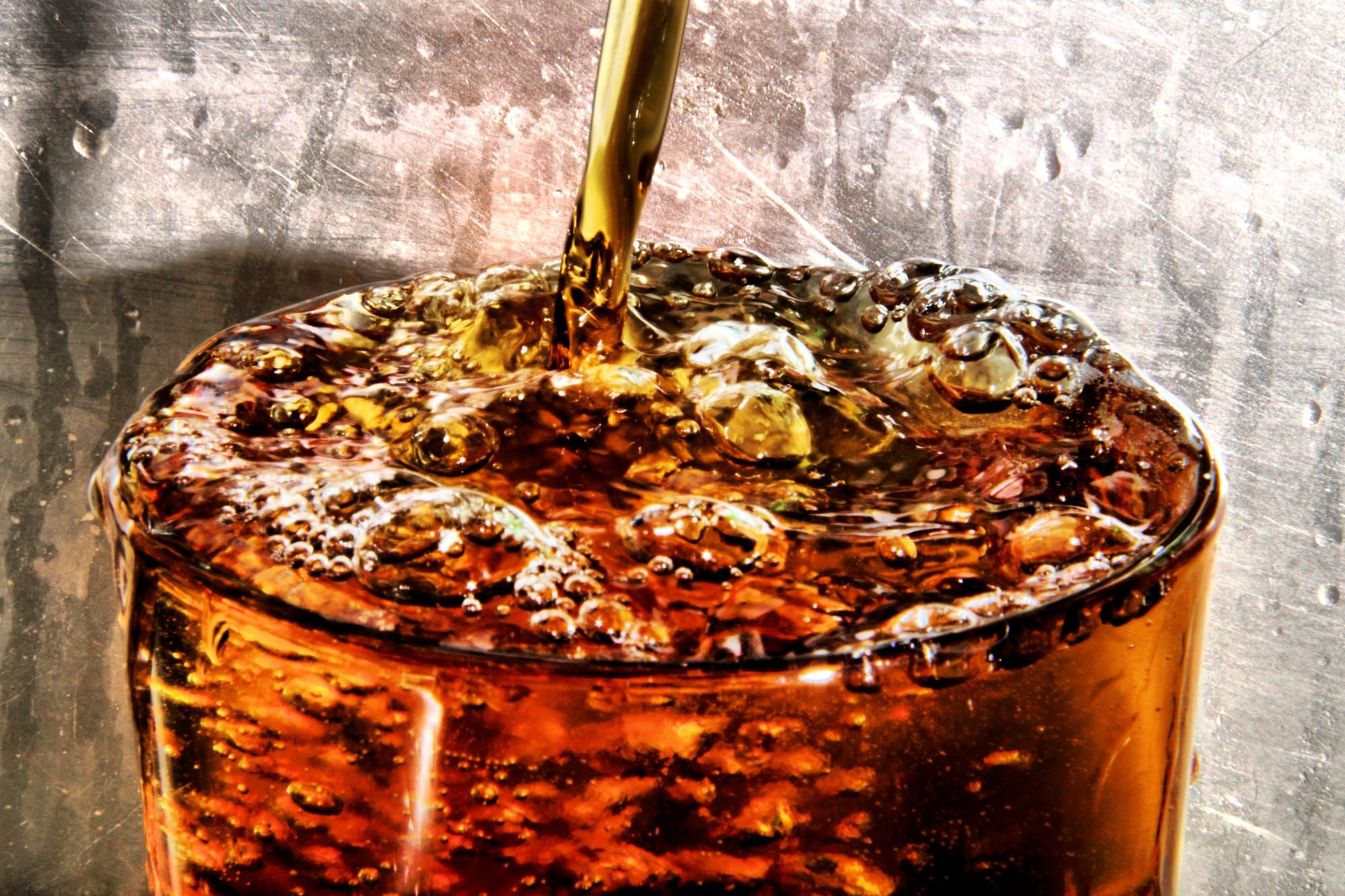 Imagen de referencia: un vaso que se llena de refresco oscuro con burbujas, sobre un fondo de metal.